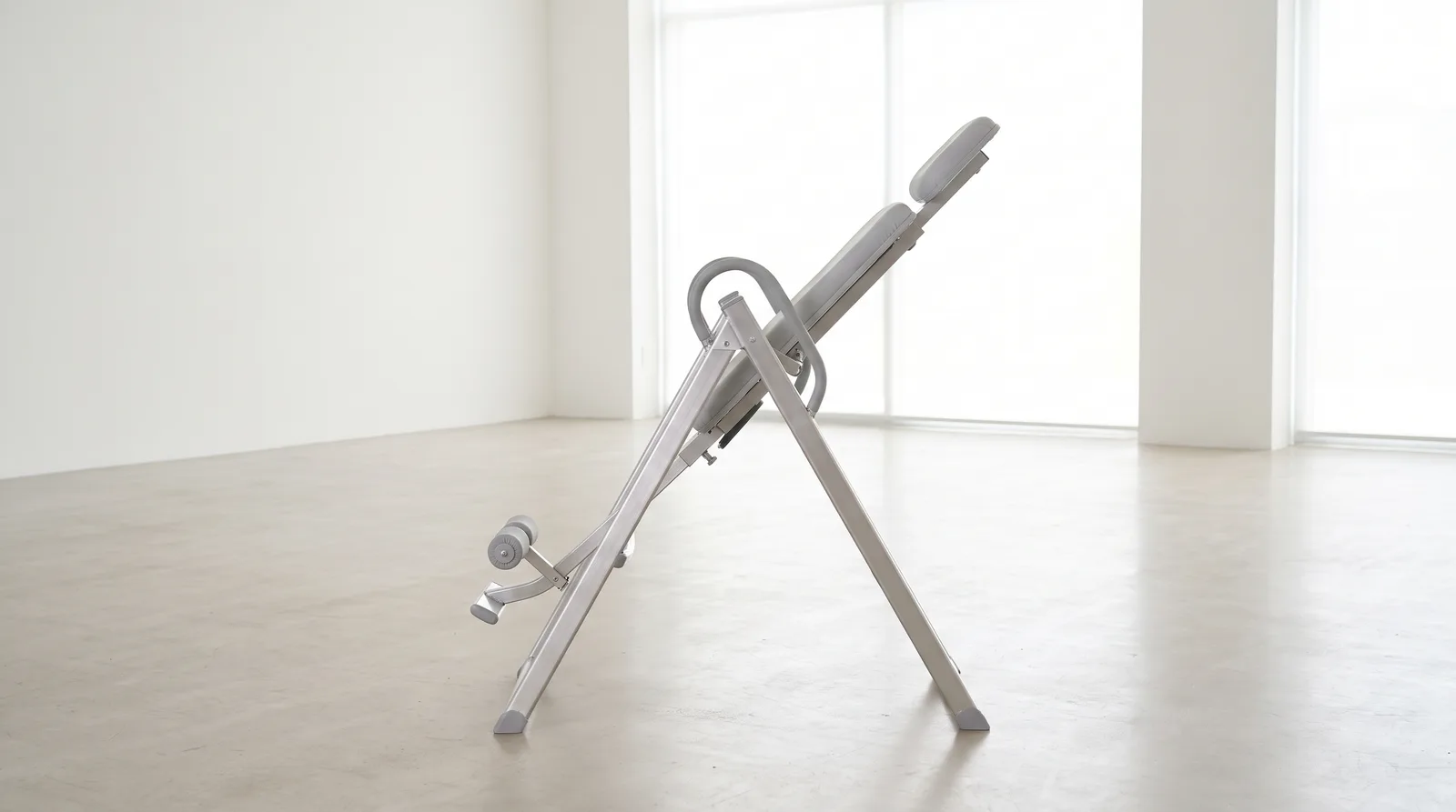 An empty inversion table tilted back in a bright minimalist room, seen from the side, clean and clinical, no text